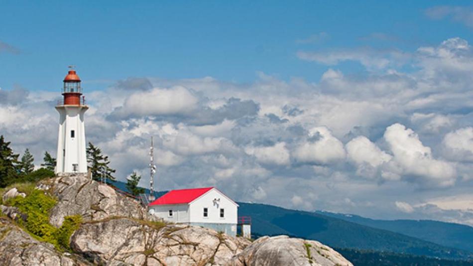 A red and white lighthouse sits on top of a large rocky hill.